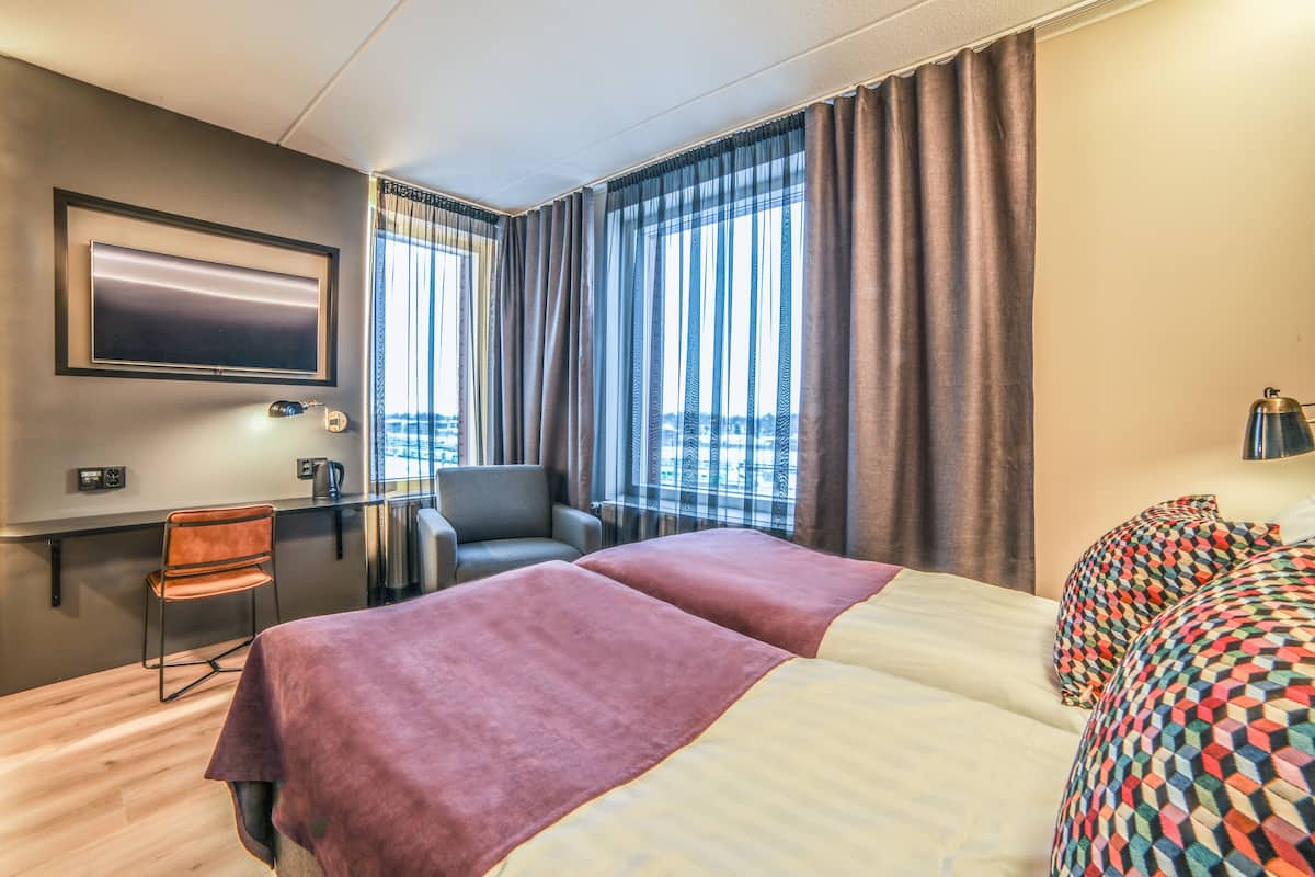 A hotel room with a bed, a desk, a chair, a TV, and a view of the city.