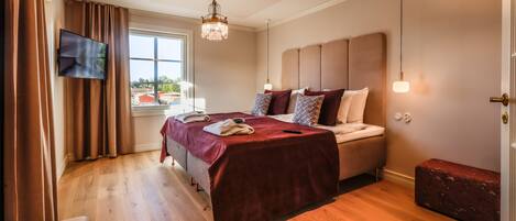 Un dormitorio con cama, televisor, candelabro y ventana con cortinas.