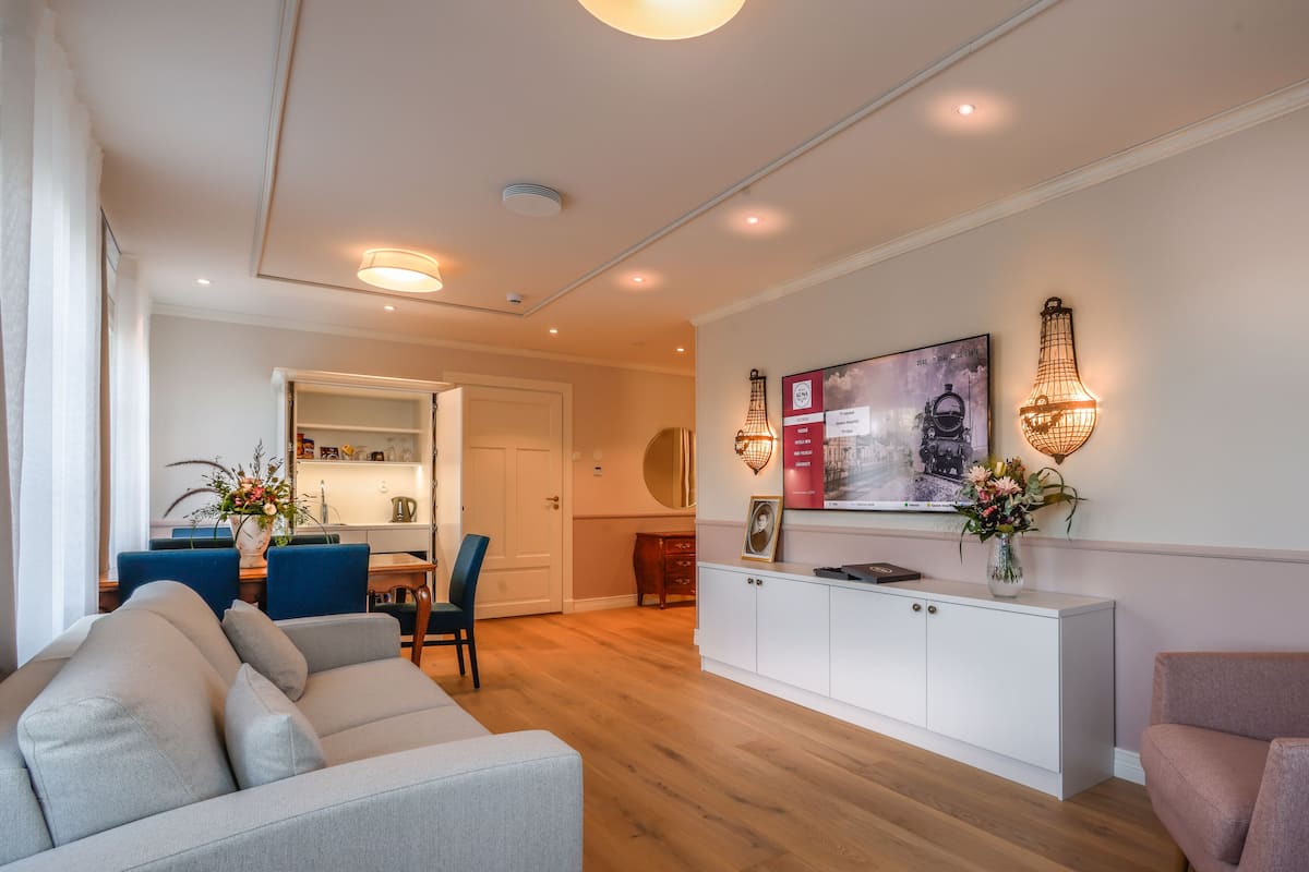 A modern living room with a sofa, a dining area with chairs, a white cabinet, and a wall-mounted TV.