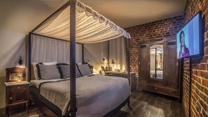 Una cama con dosel y cuatro columnas, un televisor fijado a la pared y una pared de ladrillo.