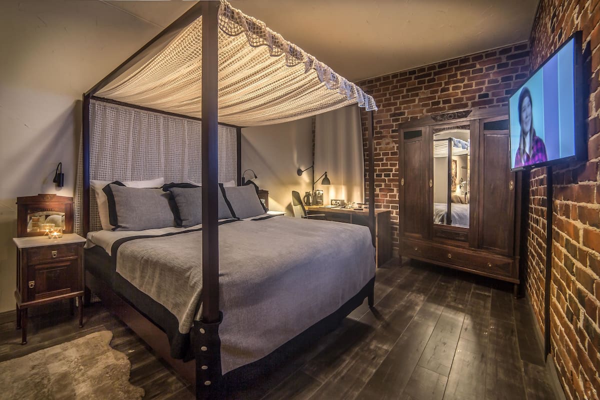 A four-poster bed with a canopy, a television mounted on the wall, and a brick wall.