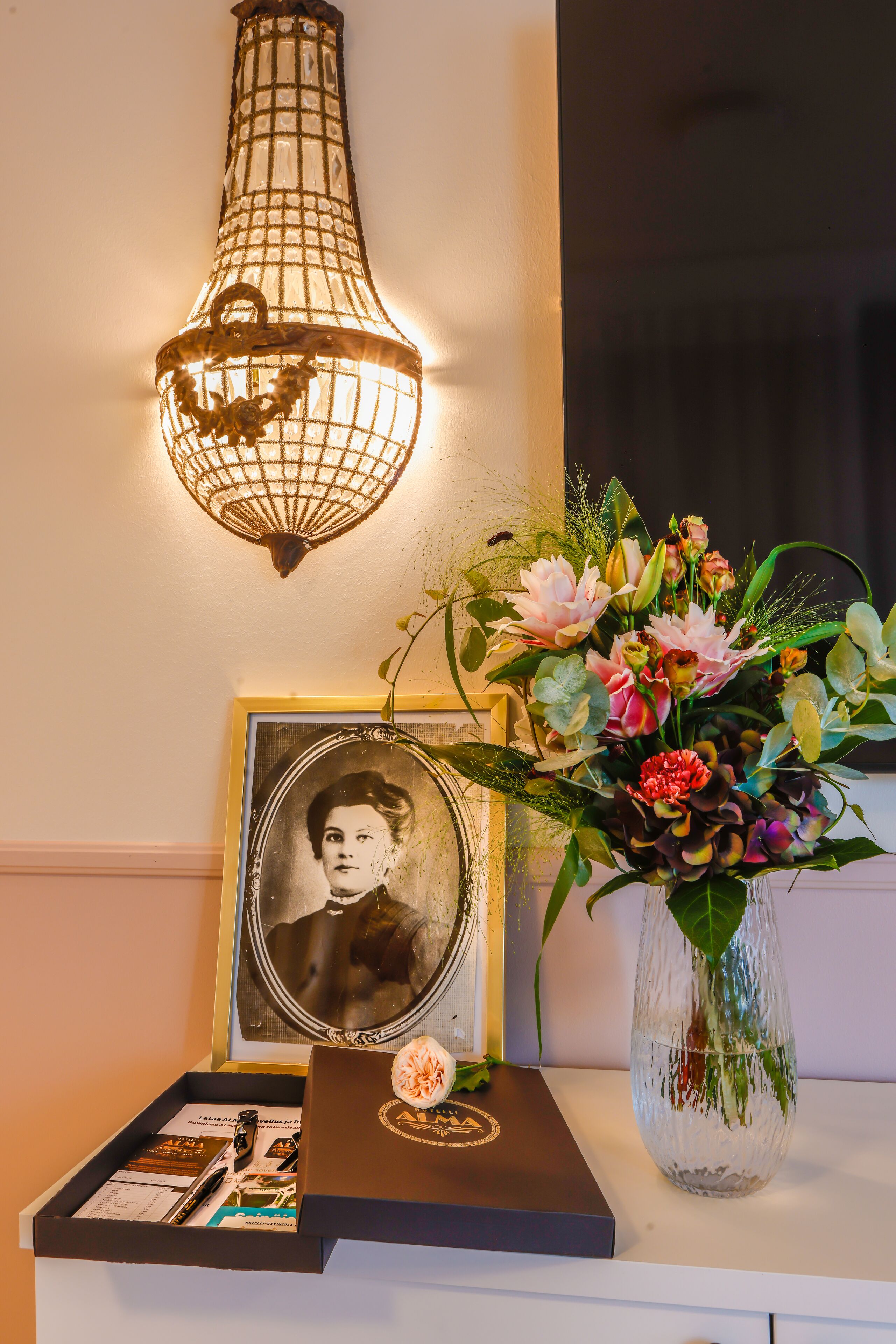 Een ingelijste foto, een vaas met bloemen en een doosje met een pen op een witte ondergrond.