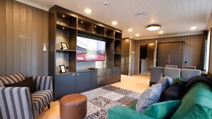Una sala de estar moderna con un televisor de pantalla plana, paneles de madera oscura, sofás a rayas y una alfombra estampada.