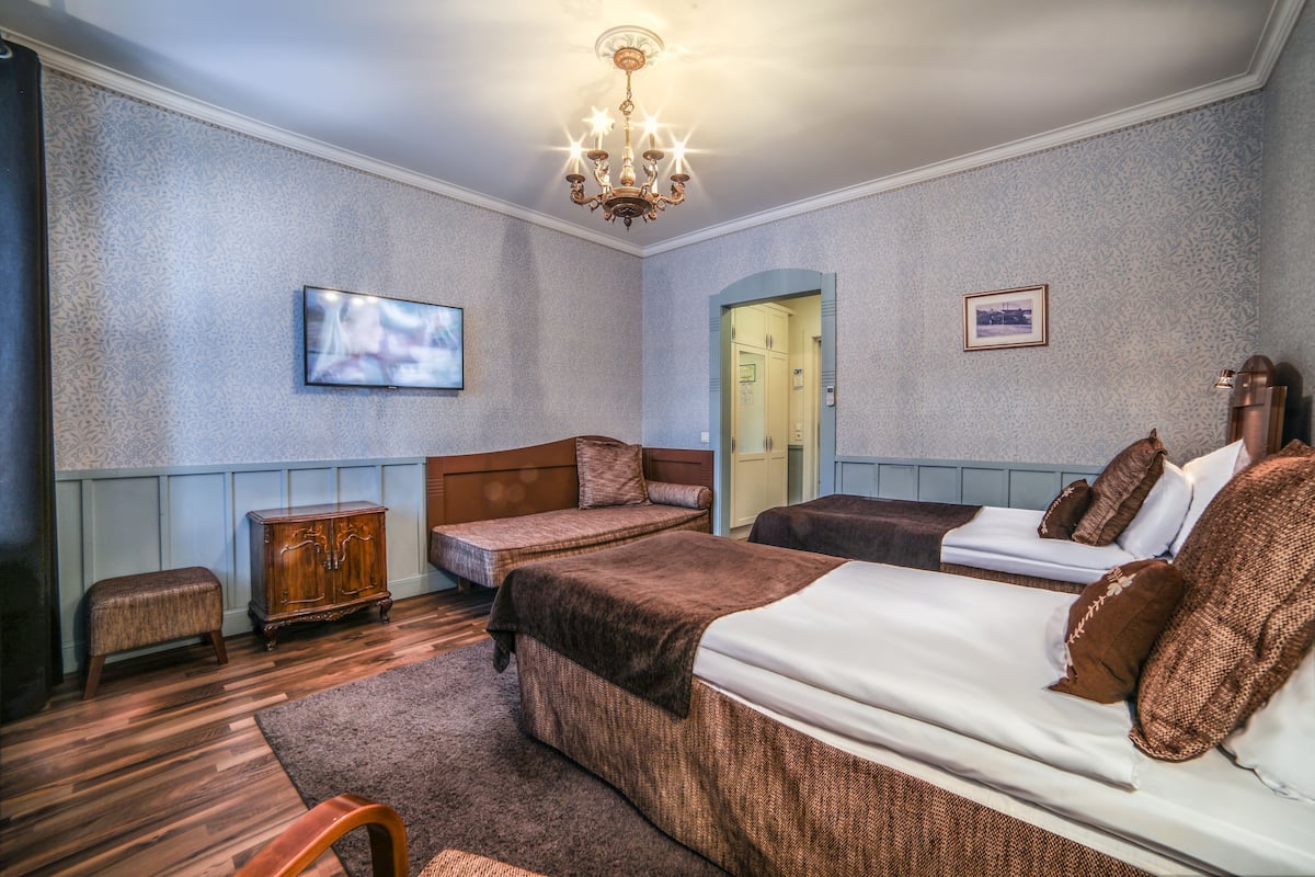 A hotel room with two beds, a television, a chandelier, and a wooden cabinet.