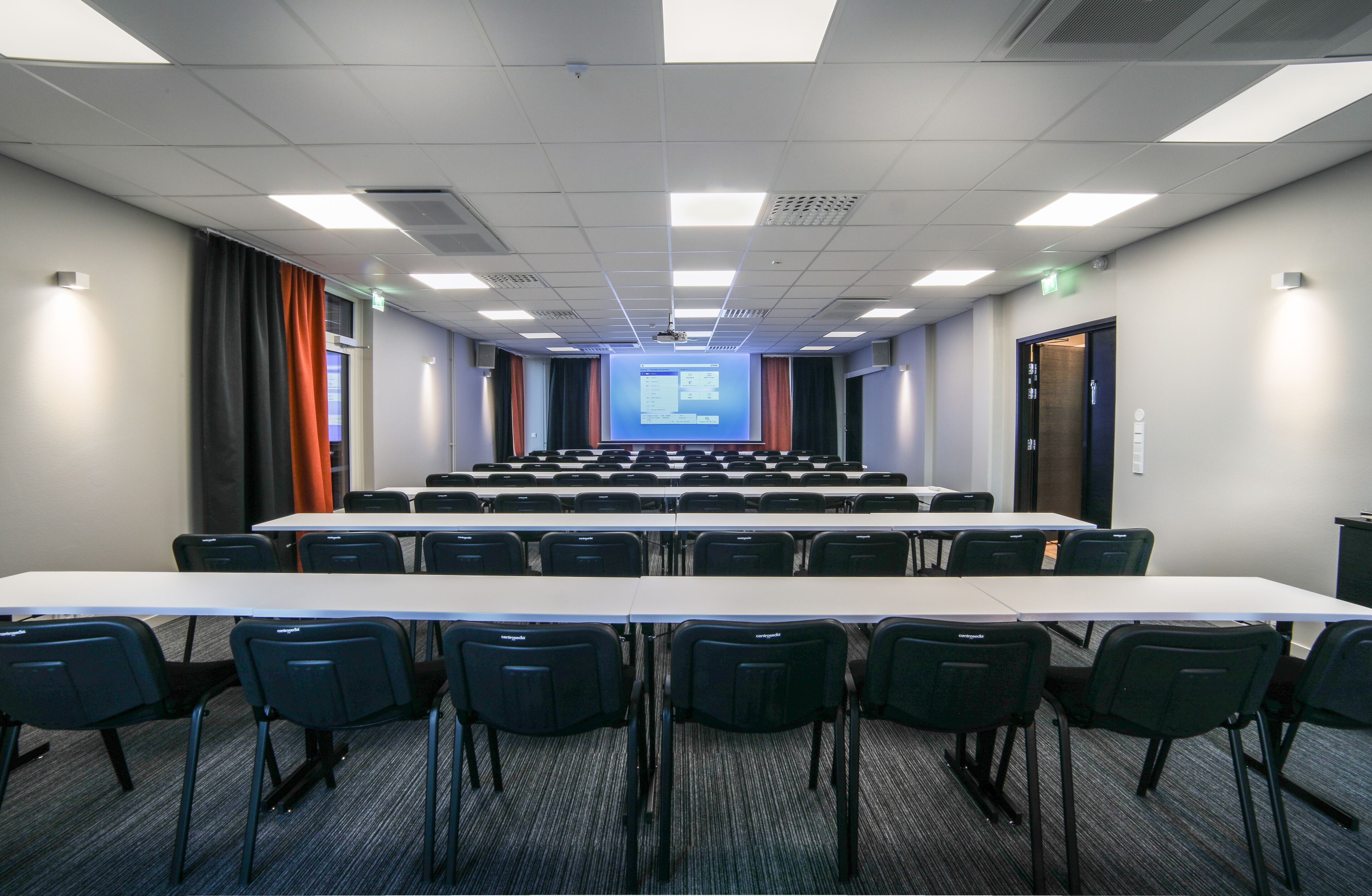A conference room with a long table and chairs, a projector screen, and a presentation slide.