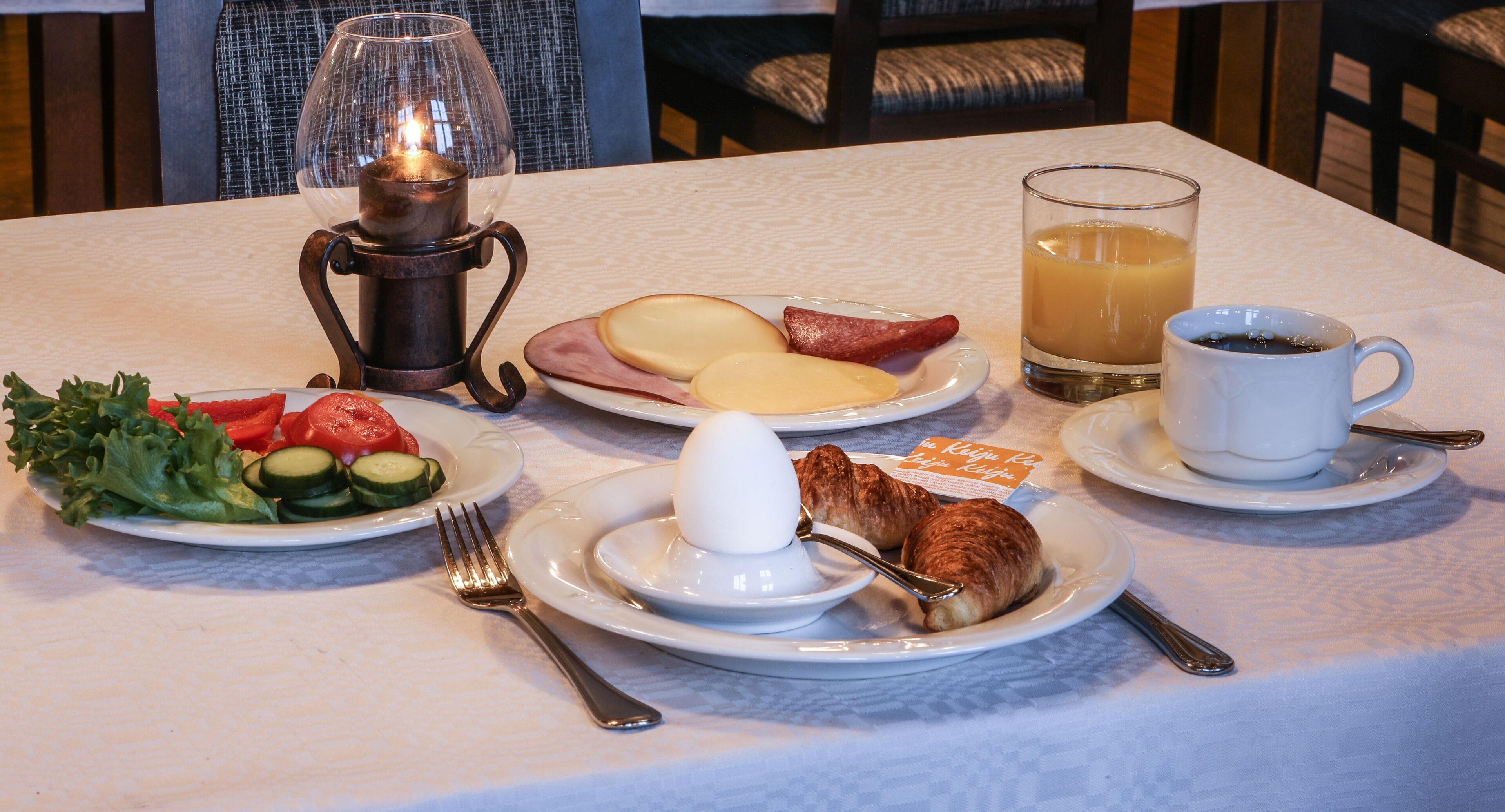 Una mesa de desayuno con platos de comida, una vela y un vaso de jugo.