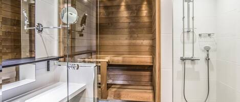 Un baño moderno con techo de madera, cabina de ducha con vidrio y lavamanos blanco.