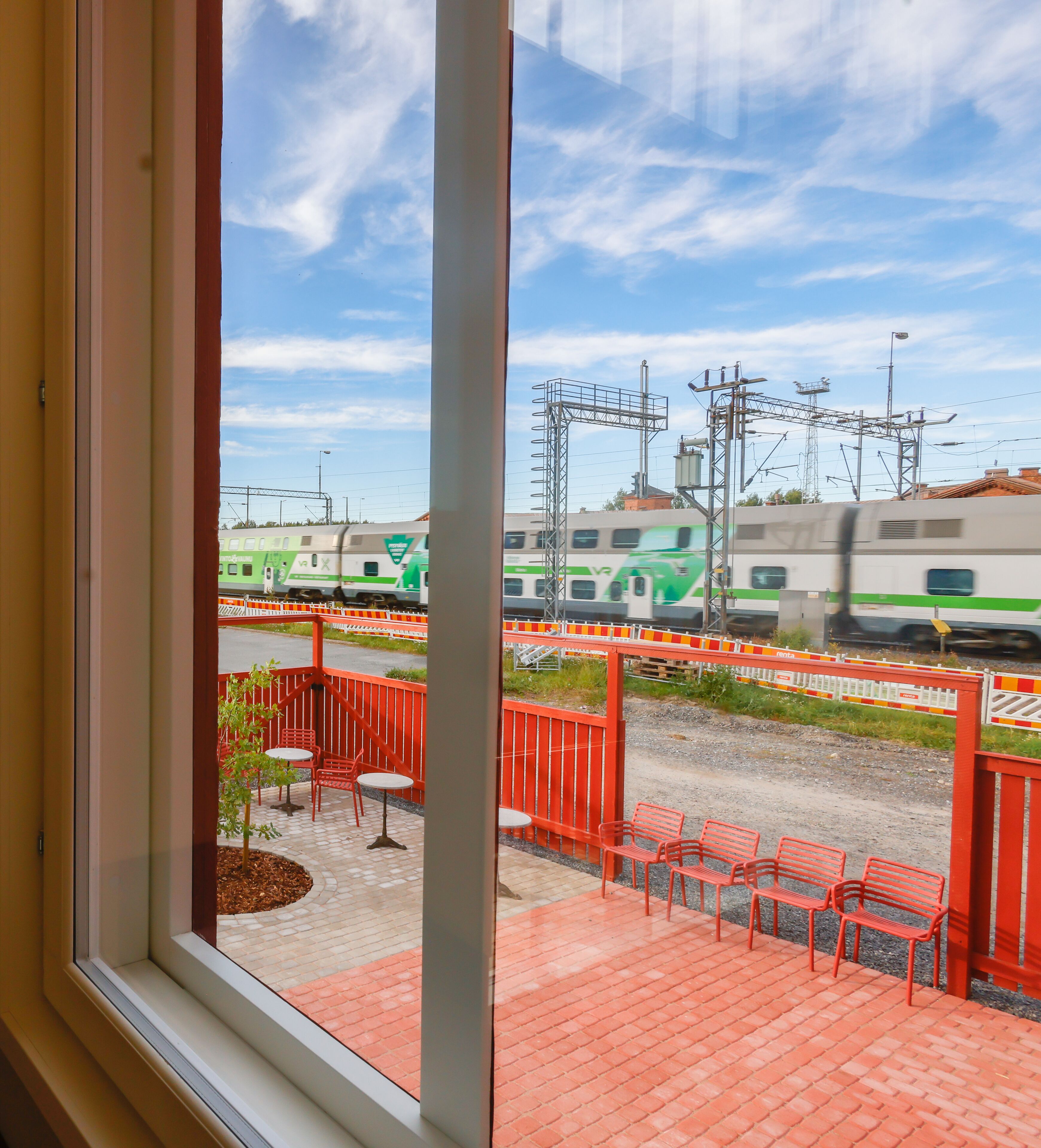 A window view of a train station platform with benches and a fence.