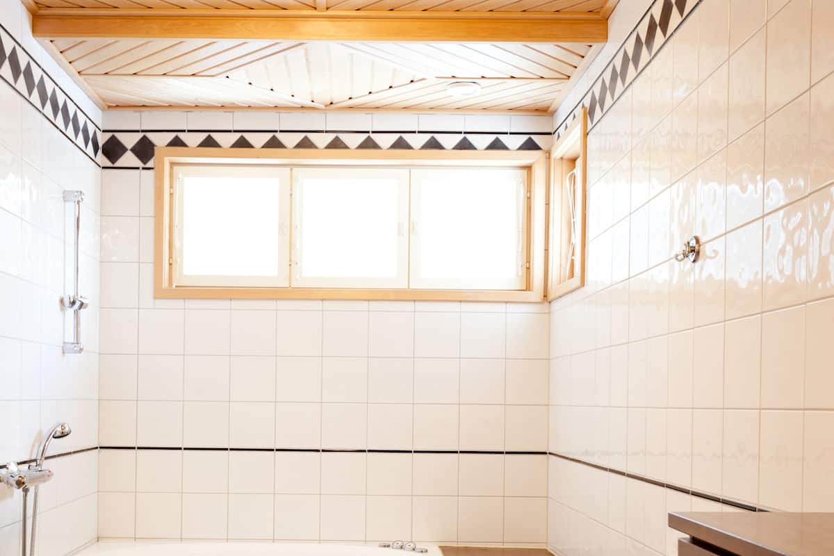 A bathroom with a checkered floor, a bathtub, wooden ceiling beams, and tiled walls.