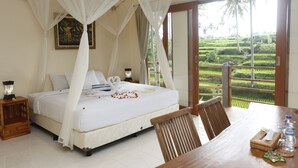 A bedroom with a bed under a canopy, a dining table with chairs, and a view of terraced fields through large windows. - Junjungan Suite Villa (Ubud)