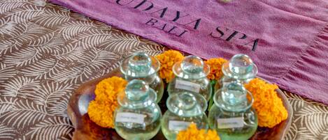 A tray of glass containers with labels, surrounded by marigold flowers, on a patterned fabric with a purple towel in the background.