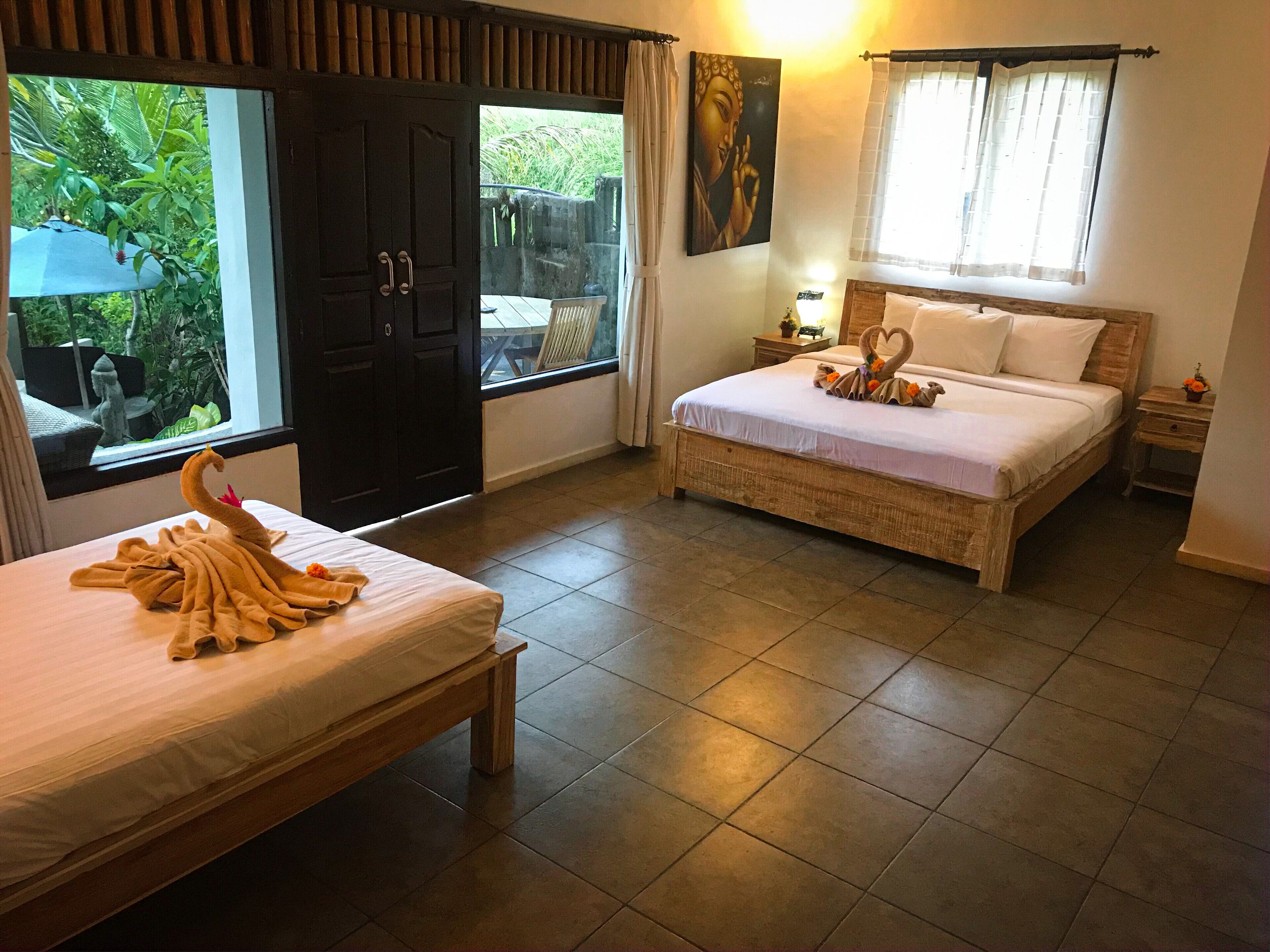 A hotel room with two beds, a large window, and a view of greenery outside.