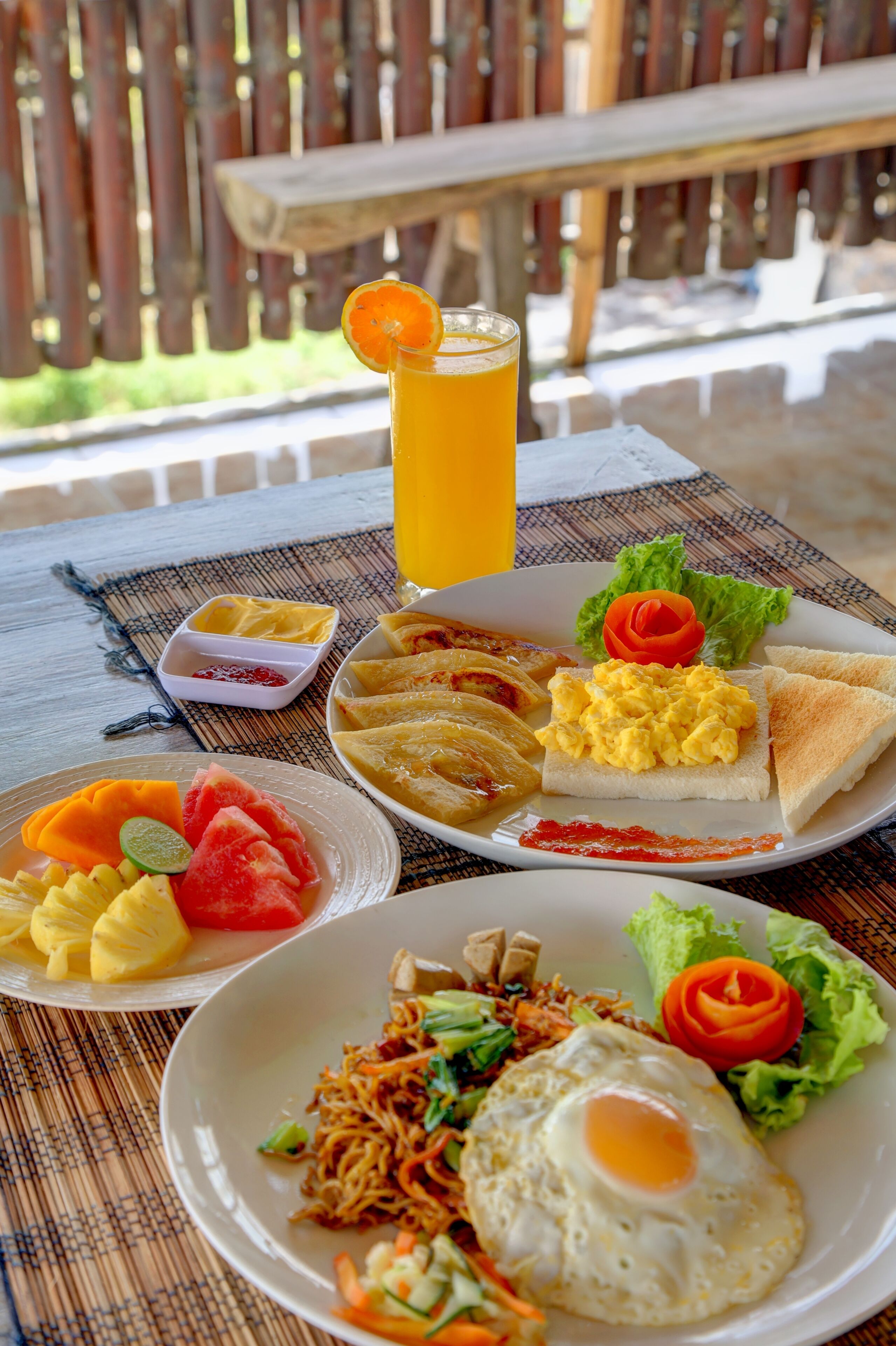 Una mesa con diversos platos, entre ellos huevos, tostadas y verduras, junto con un vaso de zumo de naranja.