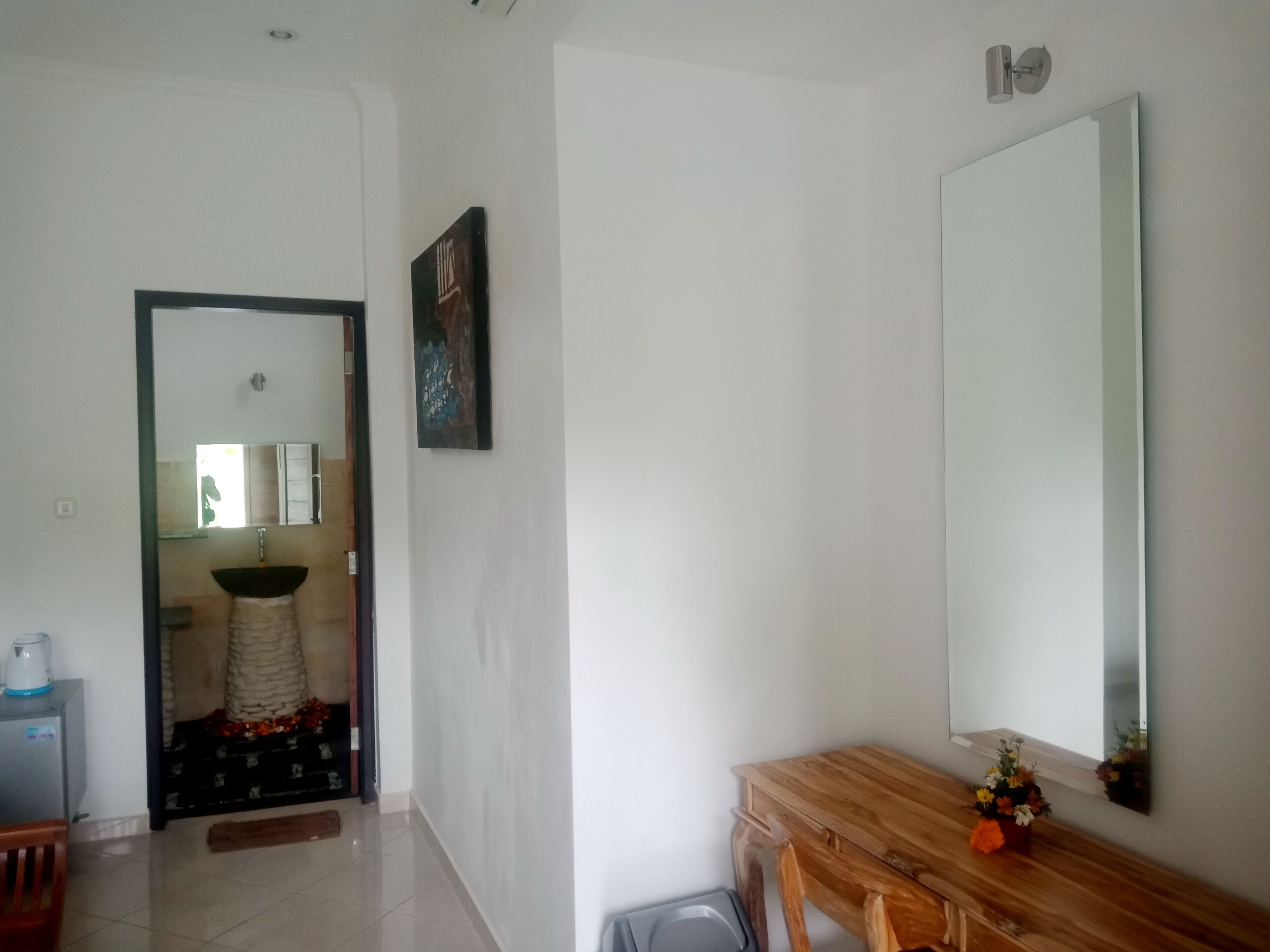A bathroom with a large mirror, a sink, and a toilet. There is a wooden bench with a vase of flowers.
