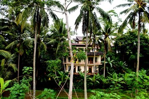 A two-story building surrounded by tall palm trees and lush greenery. - Junjungan Suite Villa (Ubud)