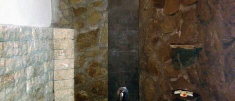 A stone-walled bathroom with a vertical water feature and a black sink.