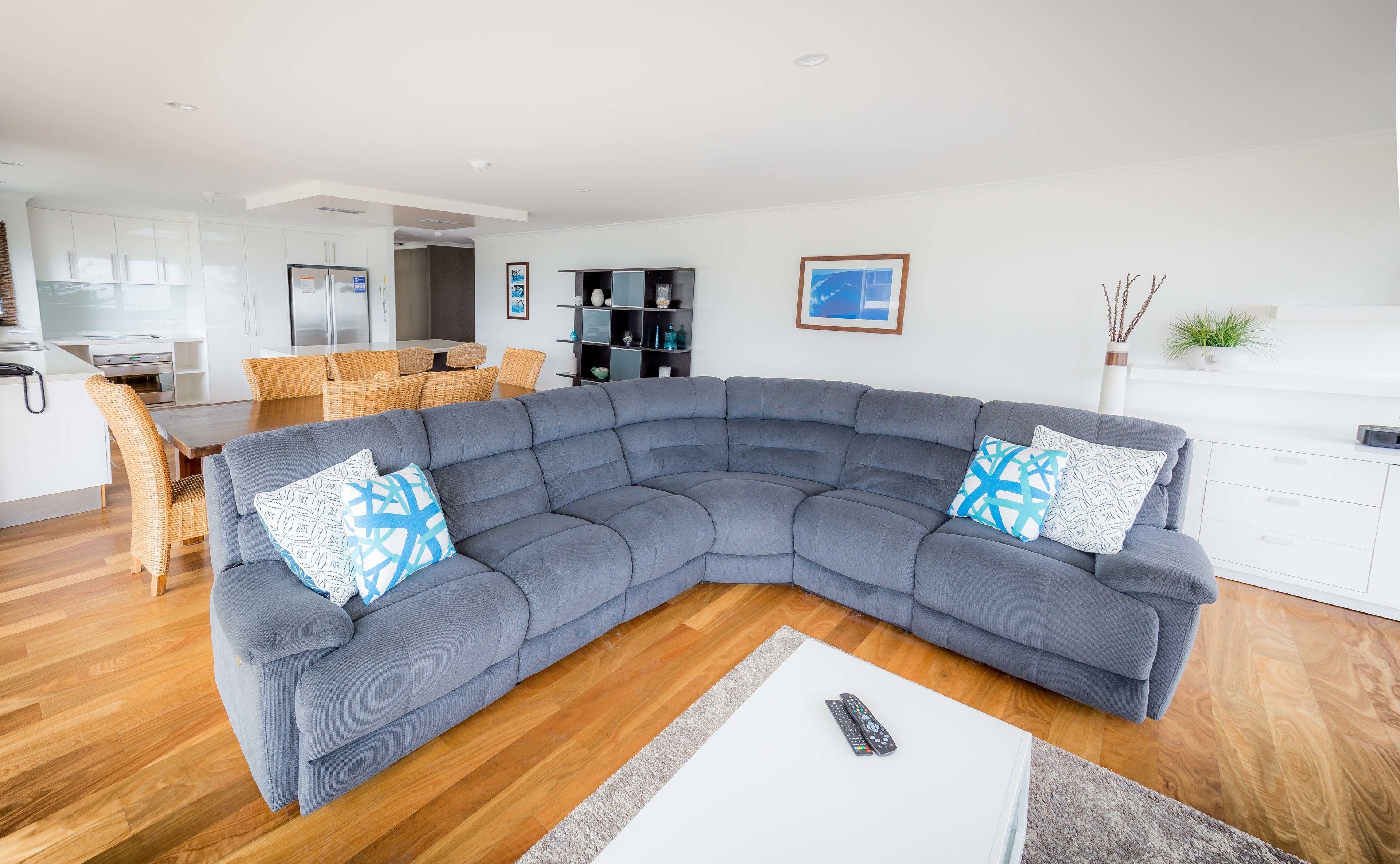 A modern living room with a grey sectional sofa, two patterned throw pillows, a white coffee table, and a remote control on it.