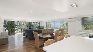 A modern kitchen with a large island, dining area with wicker chairs, and a view of the outdoors. - Solnamara Beachfront Apartments (Burleigh Heads)