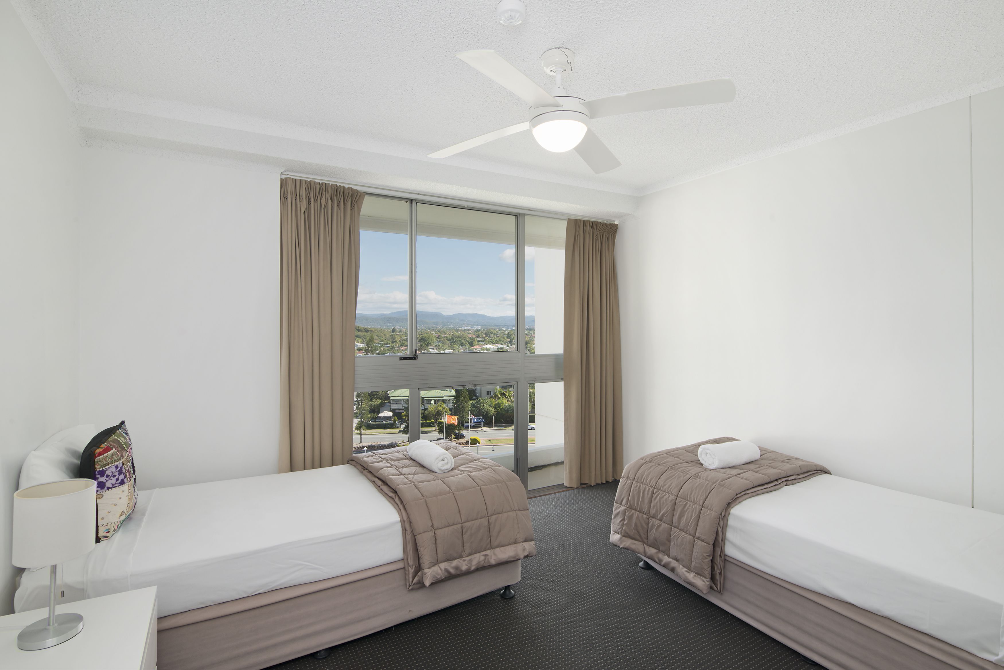 Ein Hotelzimmer mit zwei Betten, einem Deckenventilator und einem großen Fenster mit Blick auf die Stadt.