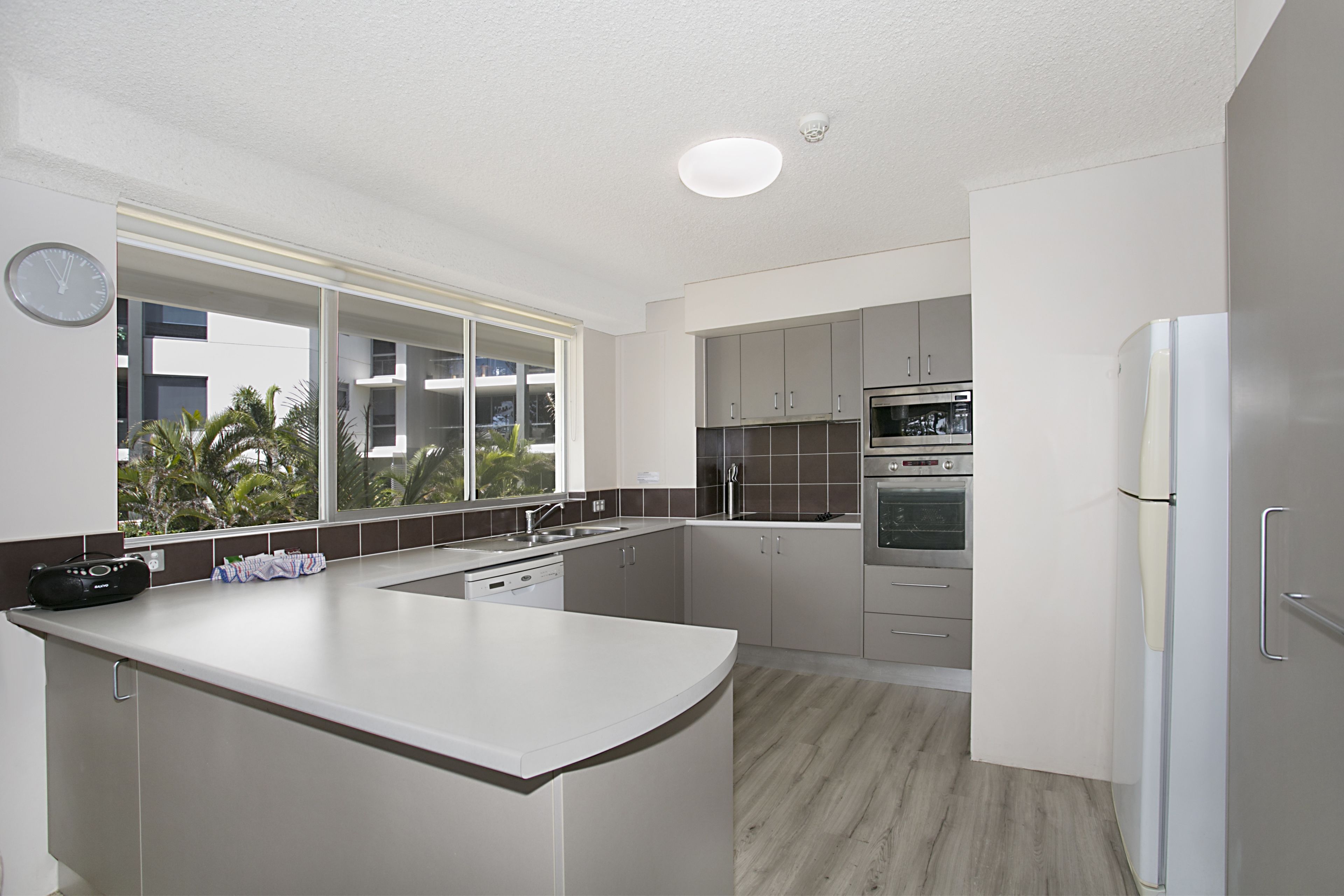 A modern kitchen with a large island, built-in appliances, and a view of palm trees outside.