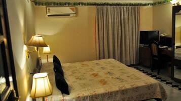Quarto de hotel com uma cama, duas luminárias de cabeceira, uma televisão, uma escrivaninha com cadeira e um aparelho de ar condicionado.