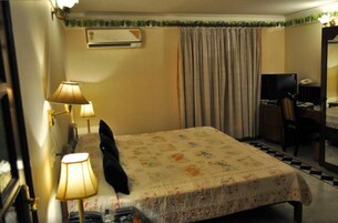 Quarto de hotel com uma cama, duas luminárias de cabeceira, uma televisão, uma escrivaninha com cadeira e um aparelho de ar condicionado.