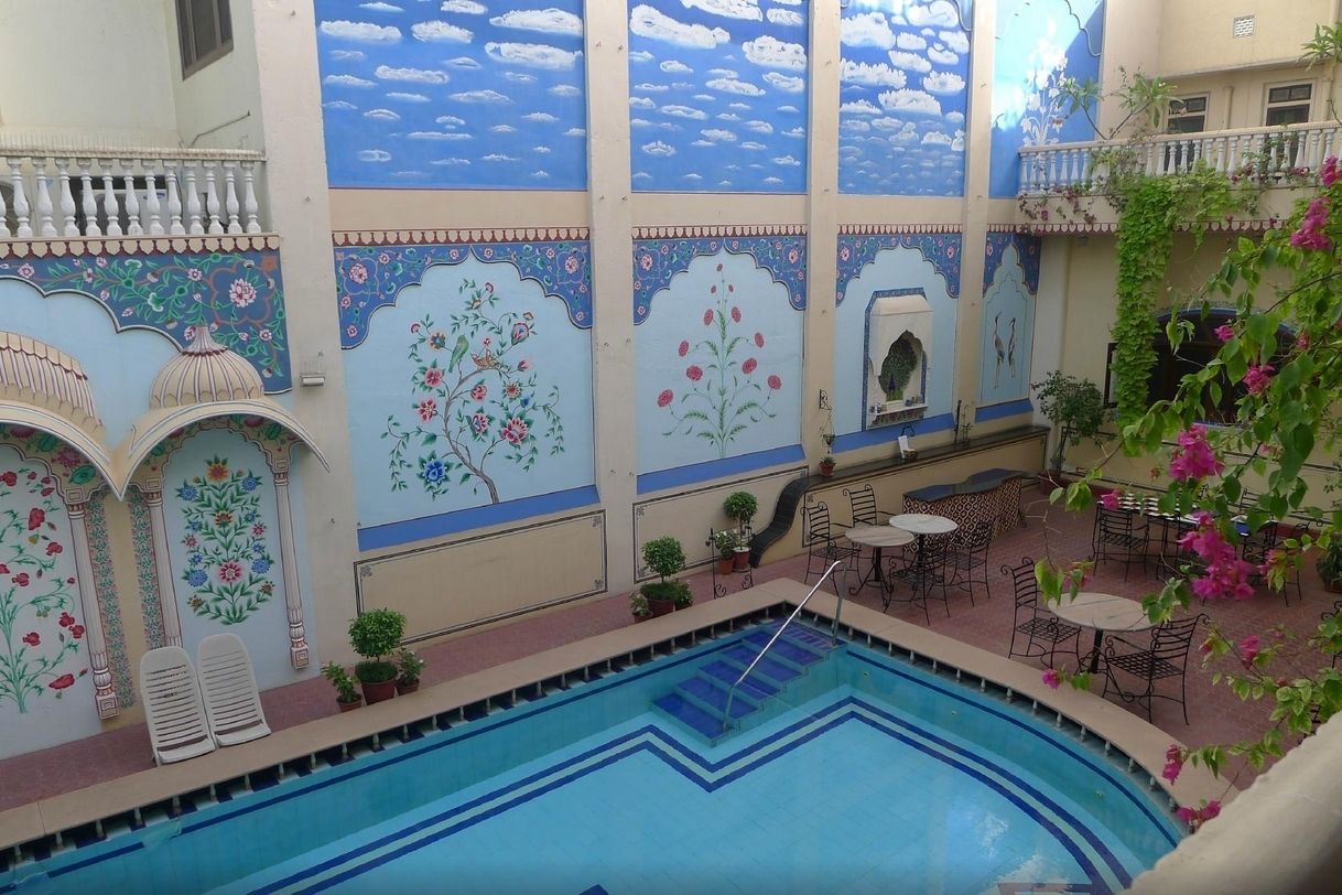 Una piscina interior con paredes de azulejos, un área de estar con mesas y sillas, y plantas en macetas.