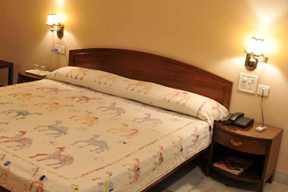 A hotel room with a bed, two wall-mounted lamps, a nightstand with a phone, and a small table with a chair.