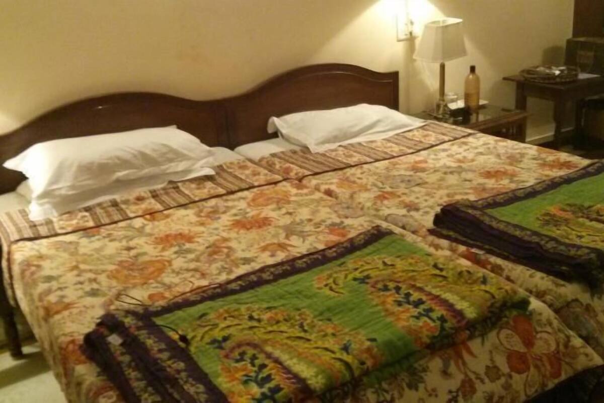 A double bed with floral bedding, a nightstand with a lamp, and a small table with a bottle.