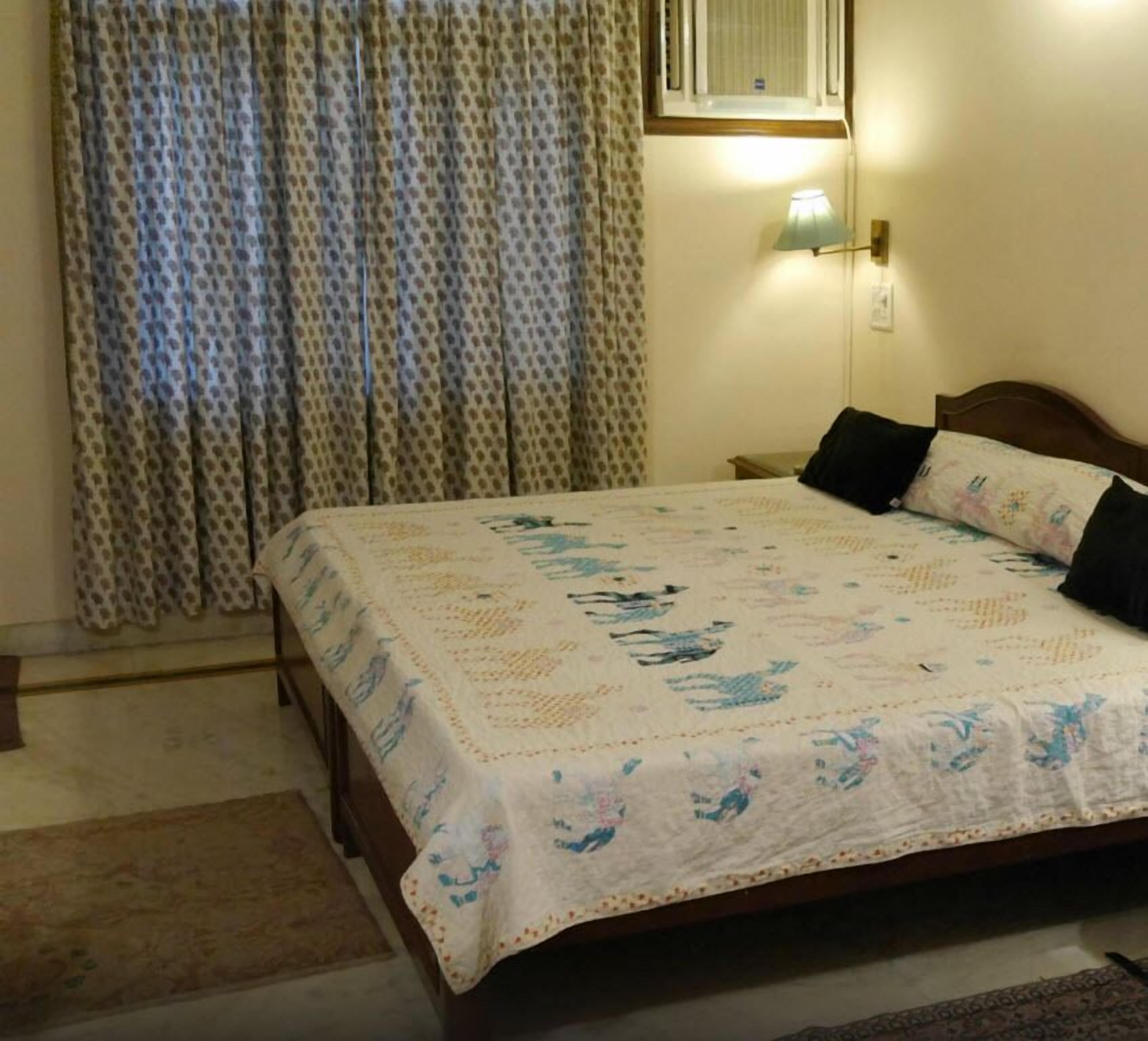 A bedroom with a bed, curtains, a nightstand, and a wall-mounted lamp.