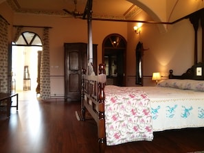 A bedroom with a four-poster bed, wooden flooring, and a large arched doorway.