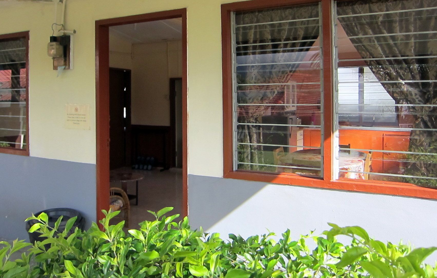 Un edificio con un gran ventanal, una puerta que da a un espacio interior y una pequeña zona exterior con plantas.