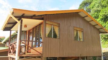 A wooden cabin with a balcony, a sloped roof, and a window with curtains.