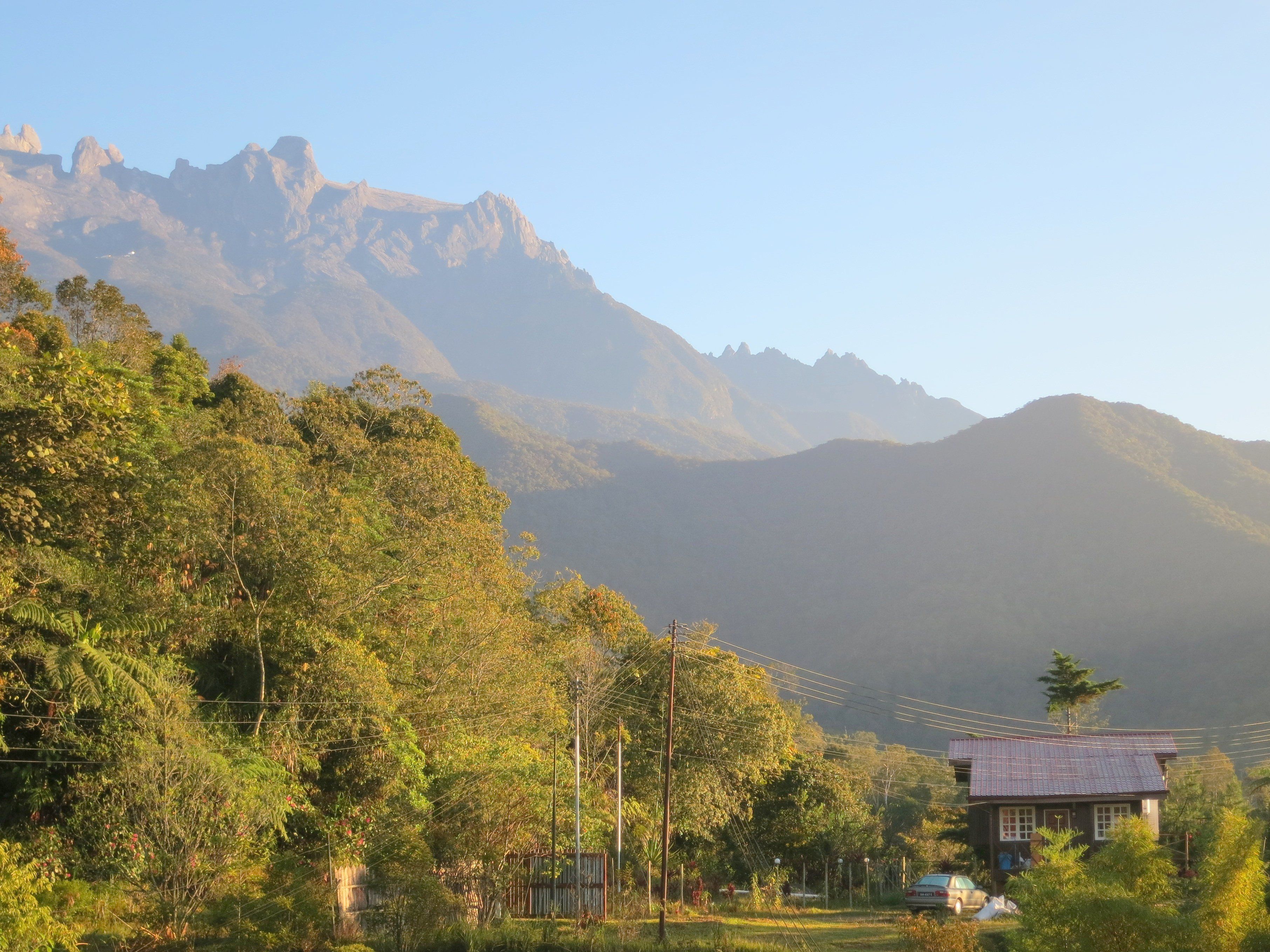A house with a tiled roof, surrounded by lush greenery and mountains in the background.