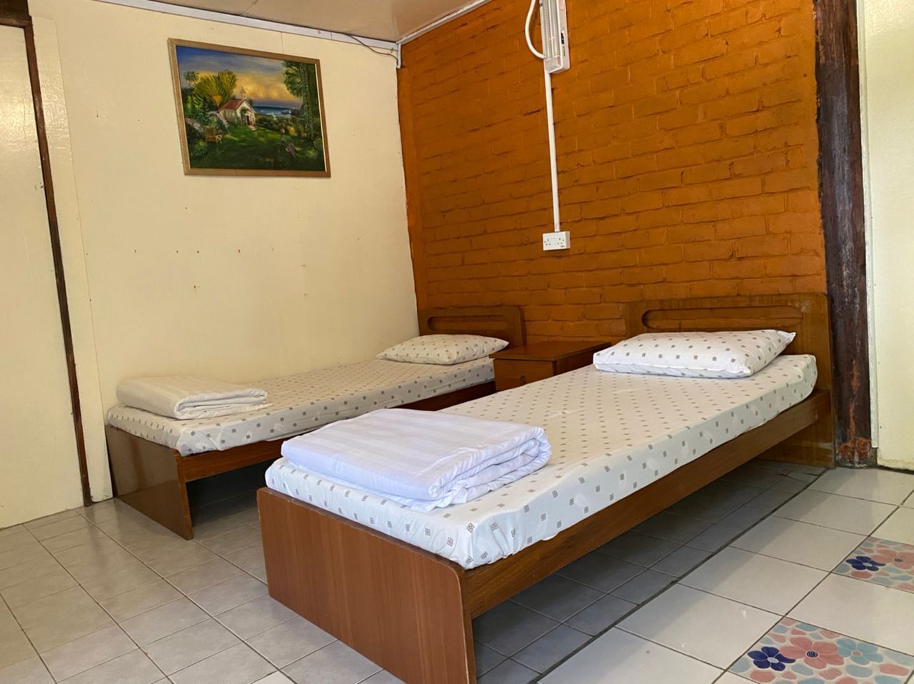 A room with two single beds, a wooden headboard, a small bedside table, and a wall-mounted power outlet.