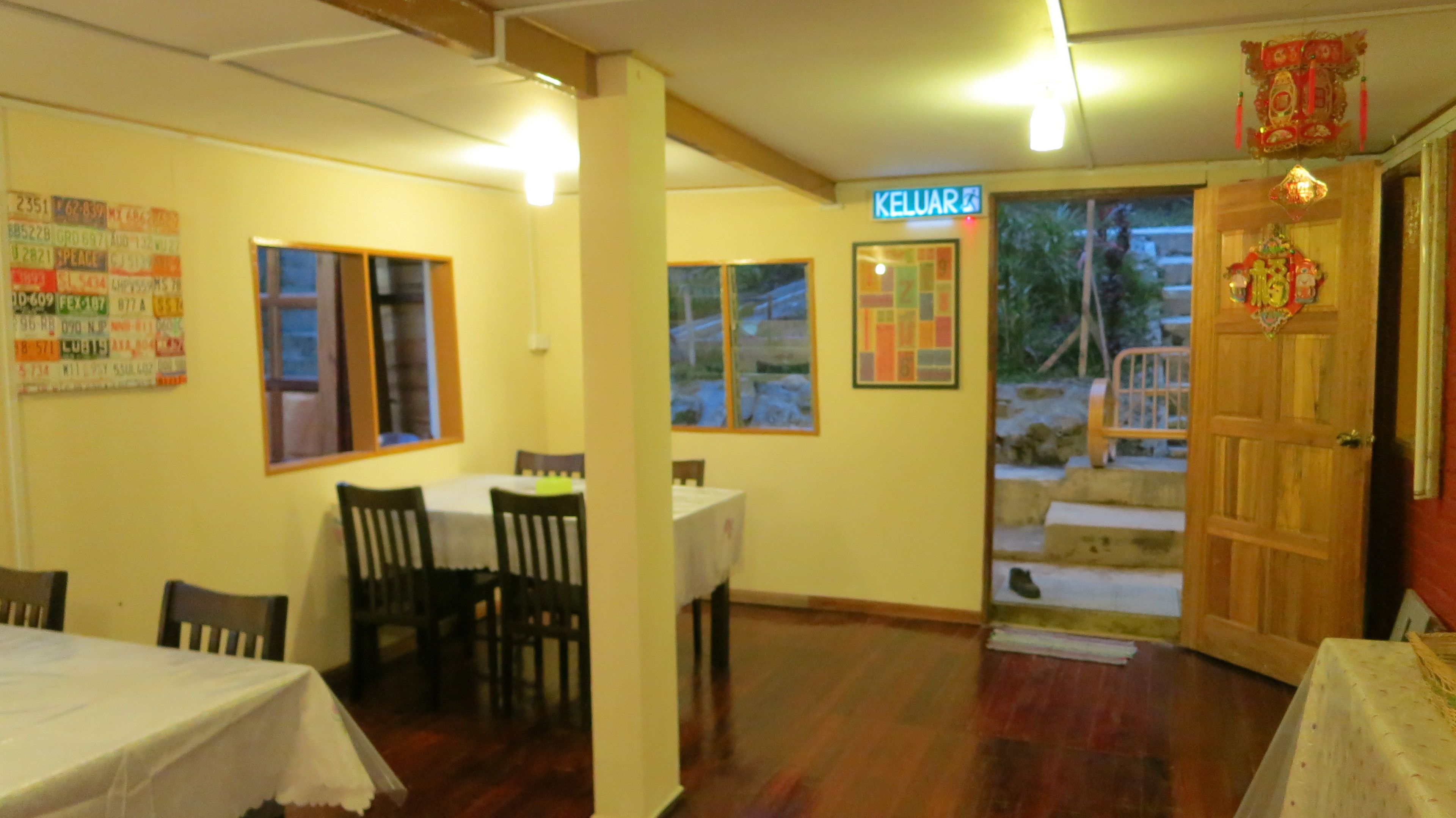 A dining area with tables and chairs, a sign reading "KELUAR", and a wooden door with a red decoration.