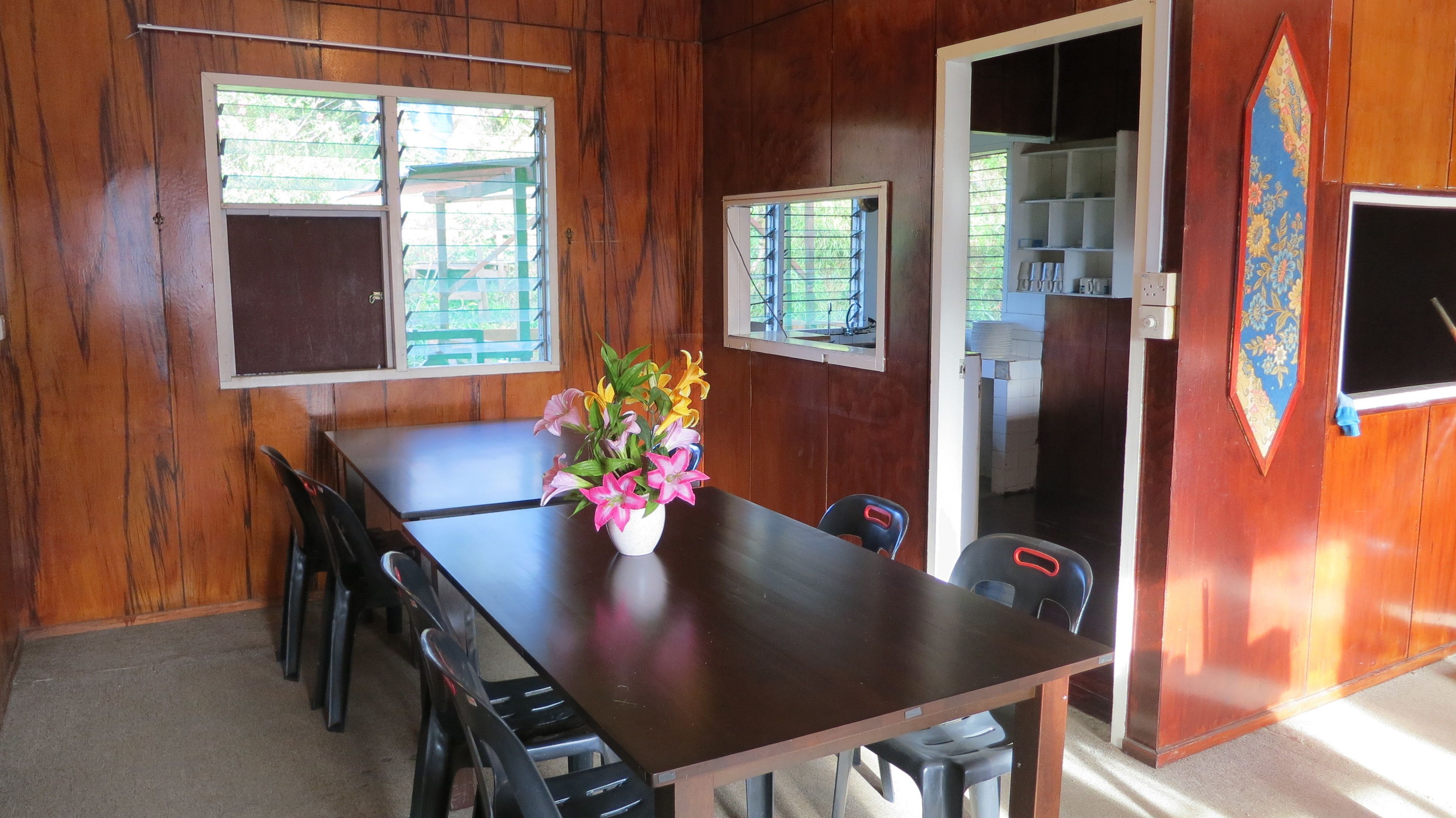 Un comedor de madera con una mesa, sillas, un florero y vistas al exterior a través de una ventana.