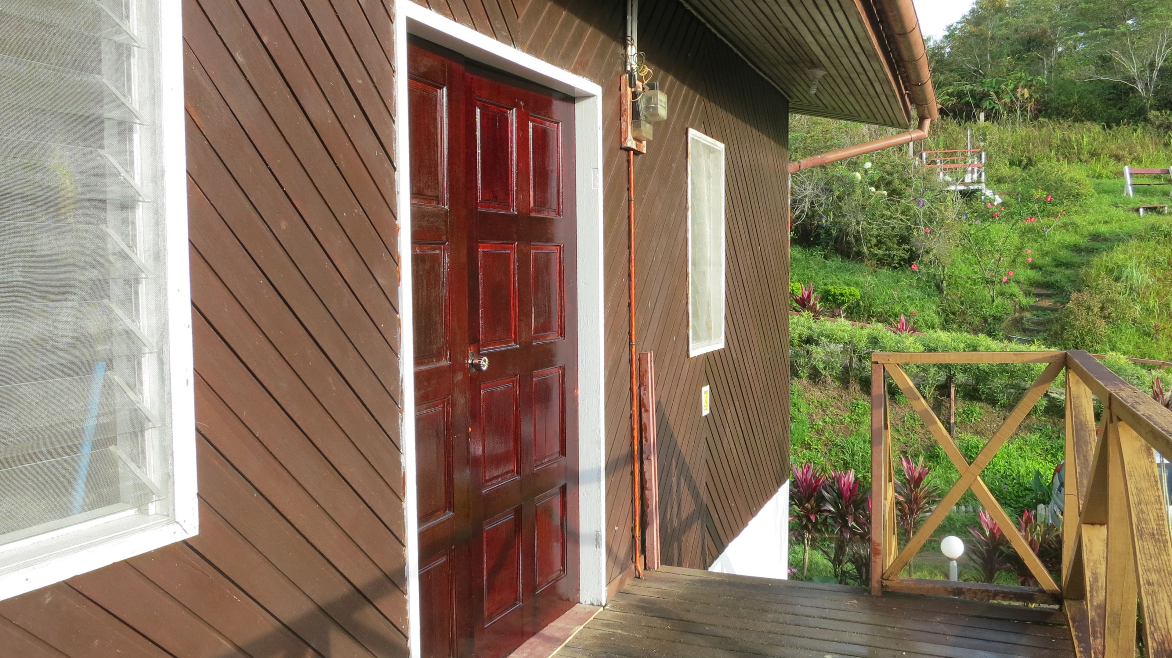 A wooden house with a red door, a small porch, and a garden with various plants and flowers.