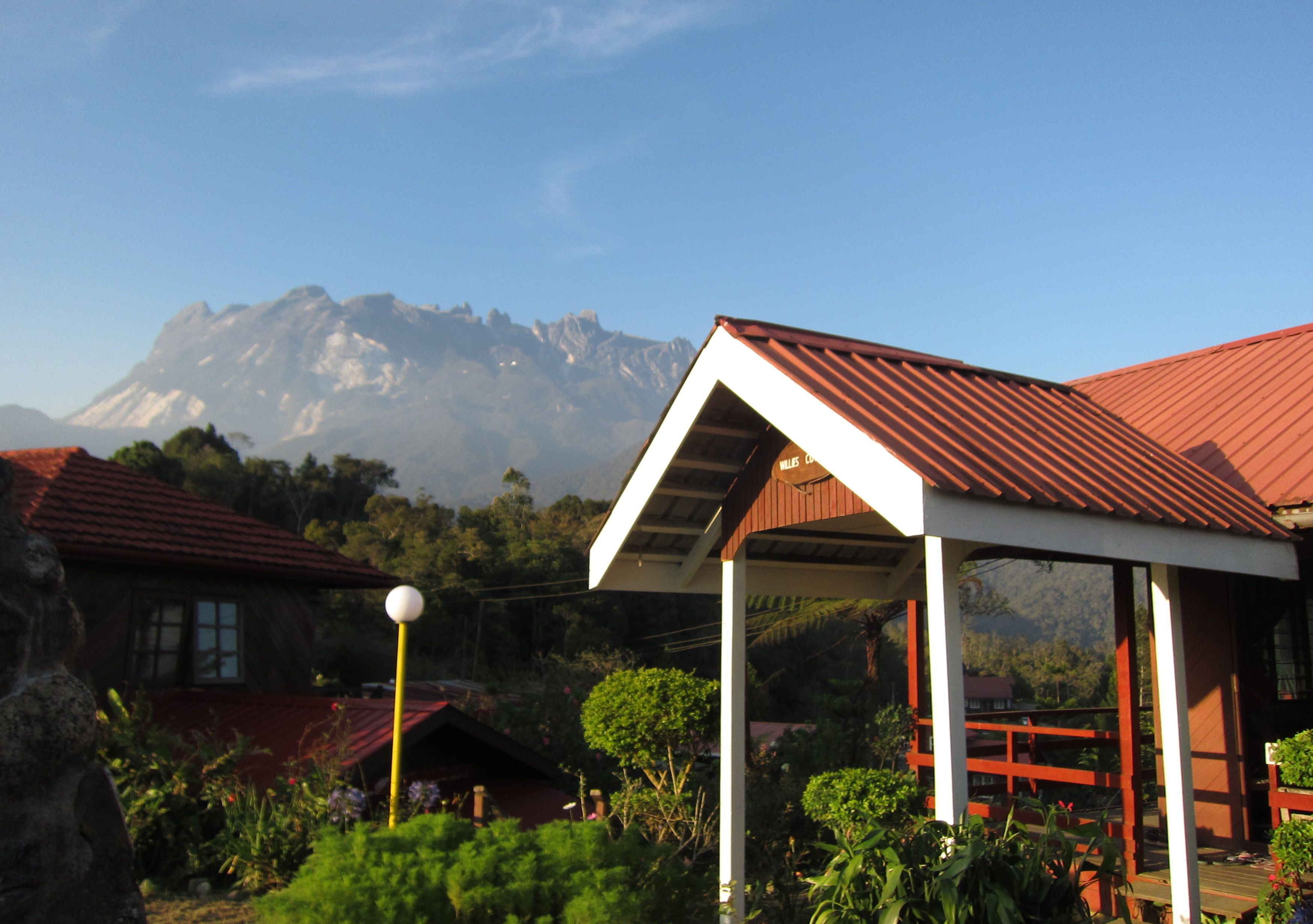 A covered outdoor area with a mountain backdrop, surrounded by greenery and buildings with red roofs.