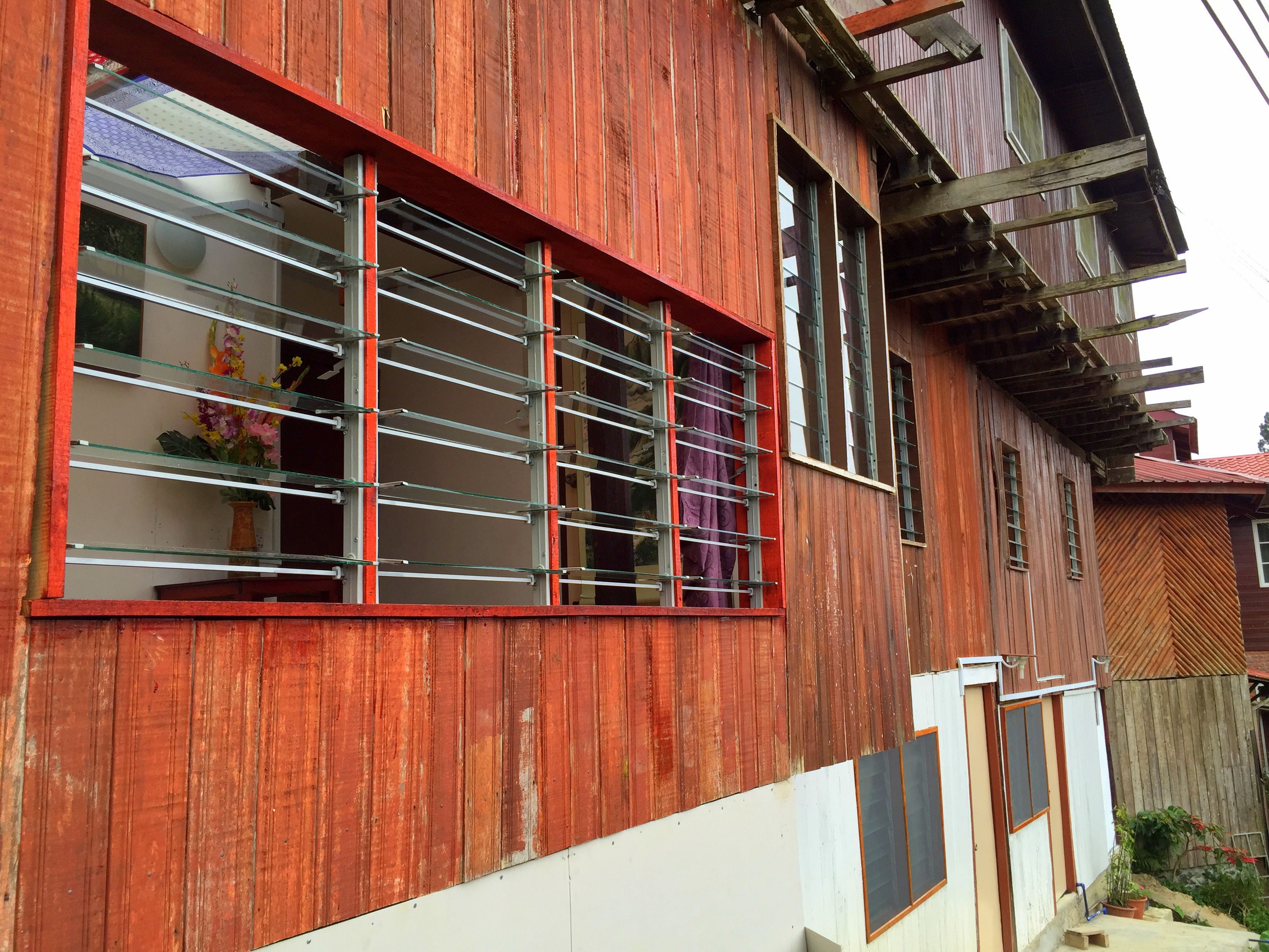 Una casa de madera con un ventanal grande que tiene barrotes de metal, una sección inferior blanca y una sección superior roja.