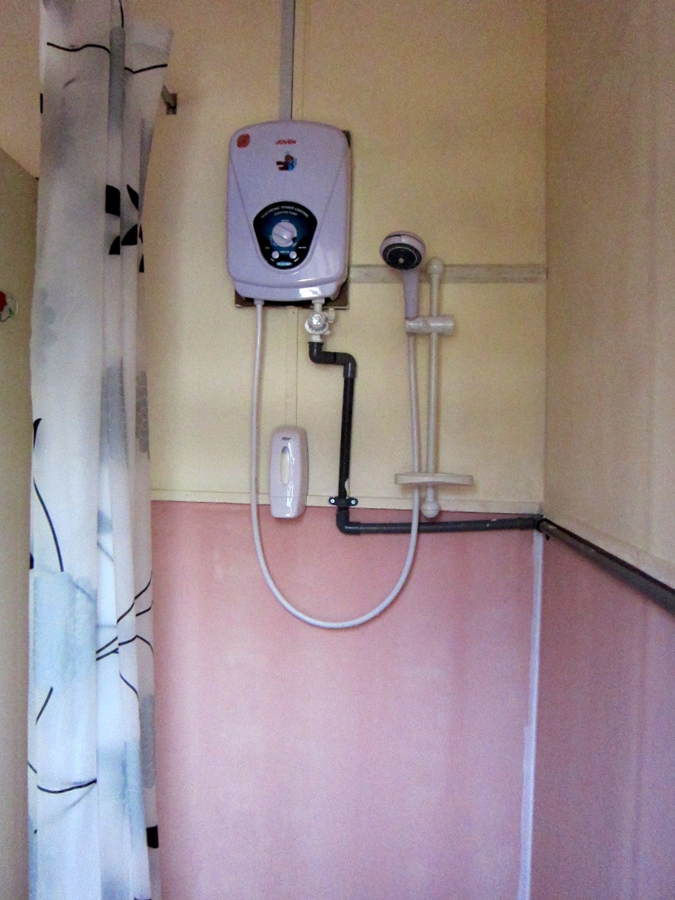 Un baño con cabina de ducha, cabezal de ducha manual y unidad de control en la pared.