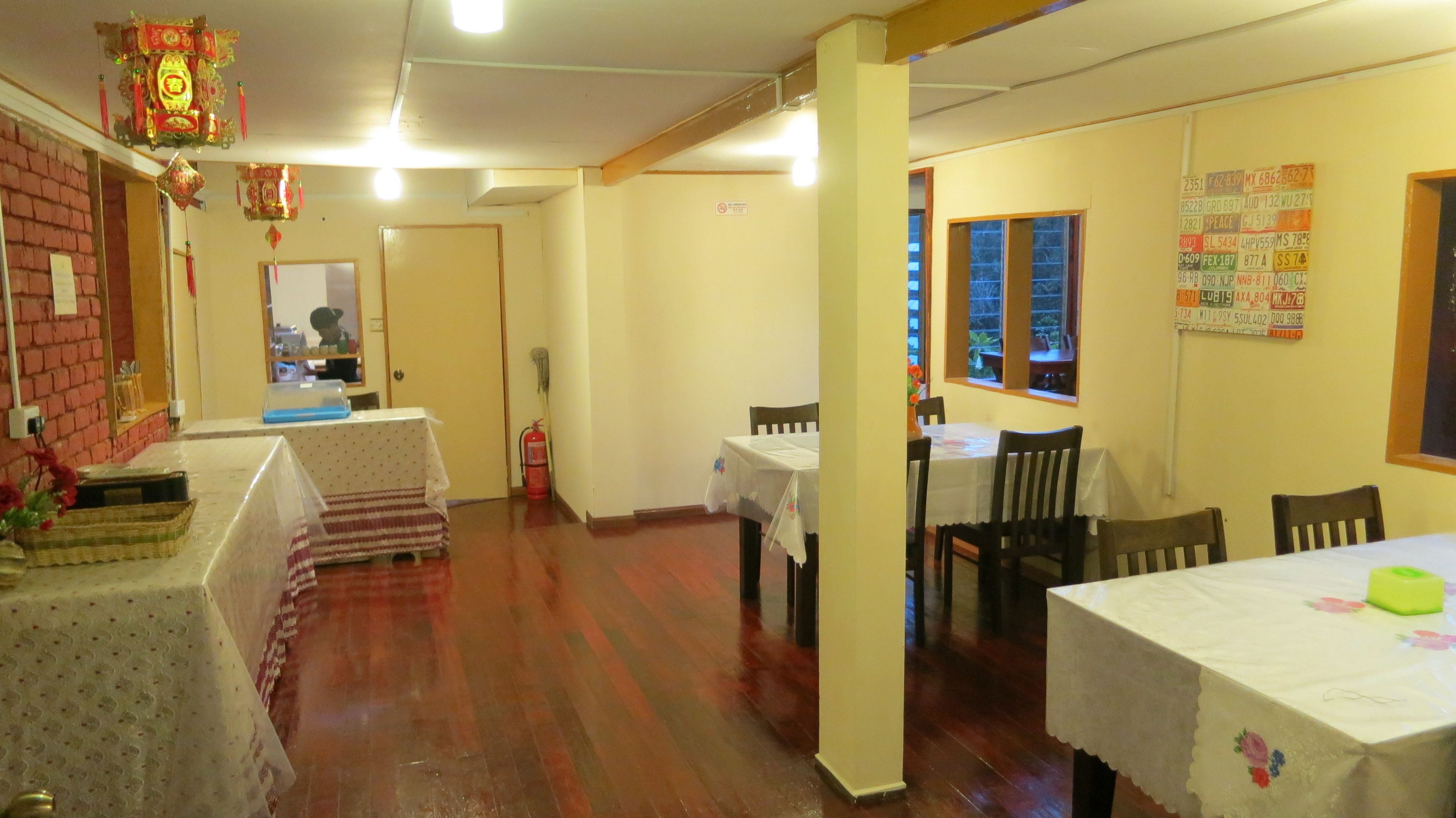 A dining area with wooden floors, tables covered with white tablecloths, and chairs. There are decorative elements on the walls and a window with a view.