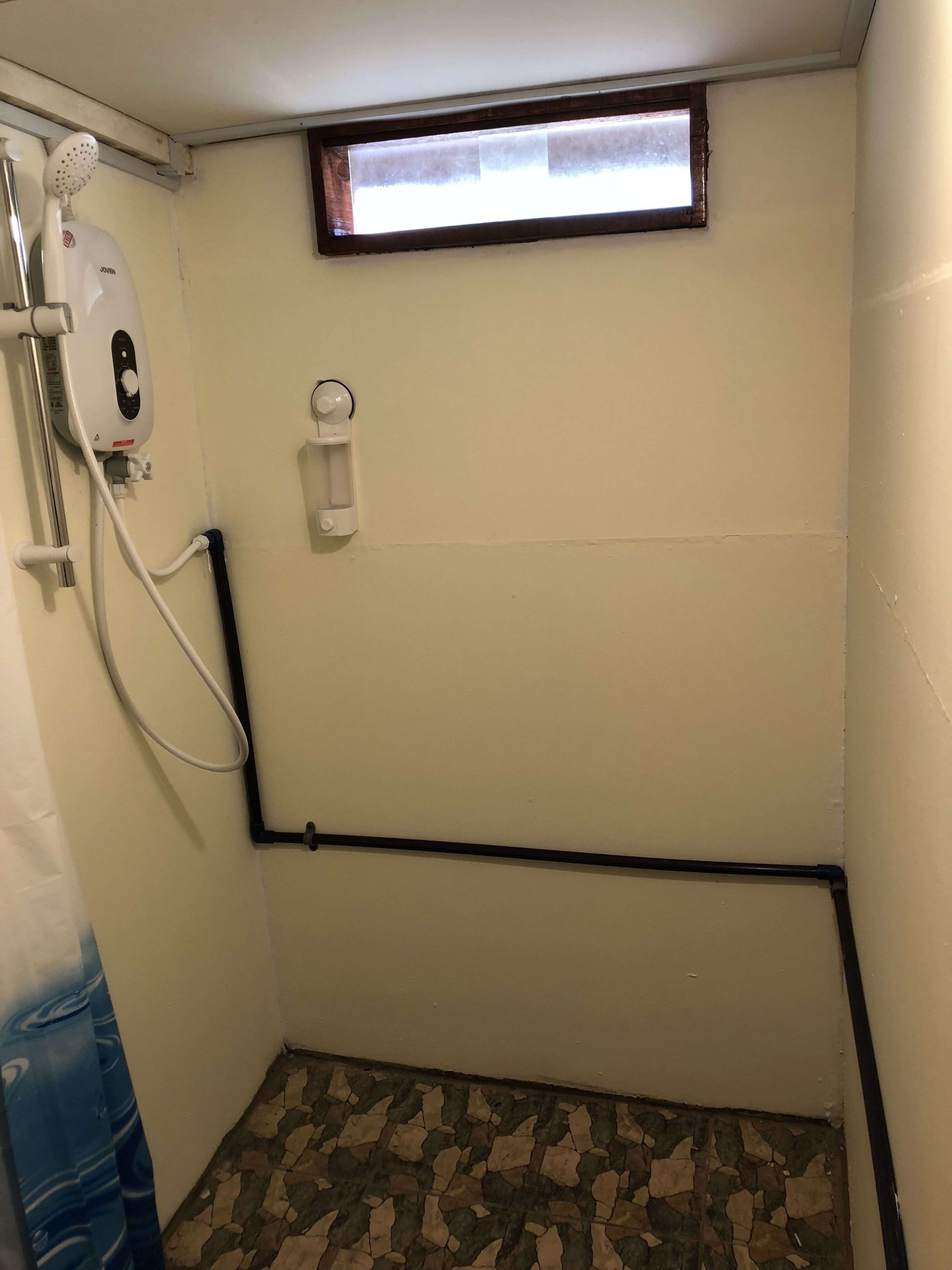 A small, enclosed bathroom with a shower, a window, and a tiled floor.