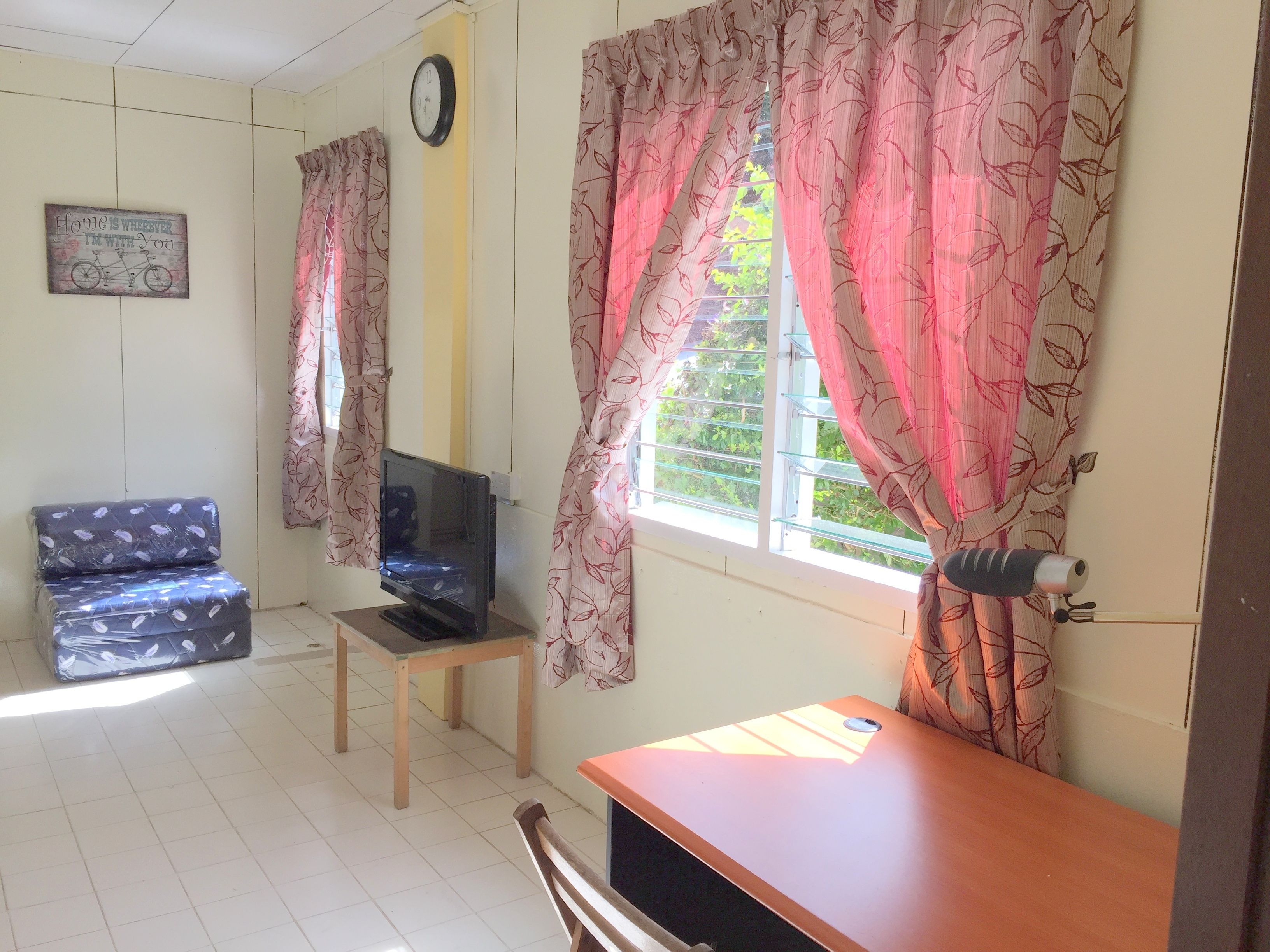 A living room with a sofa, a TV on a stand, a wooden table, and curtains with a leaf pattern.