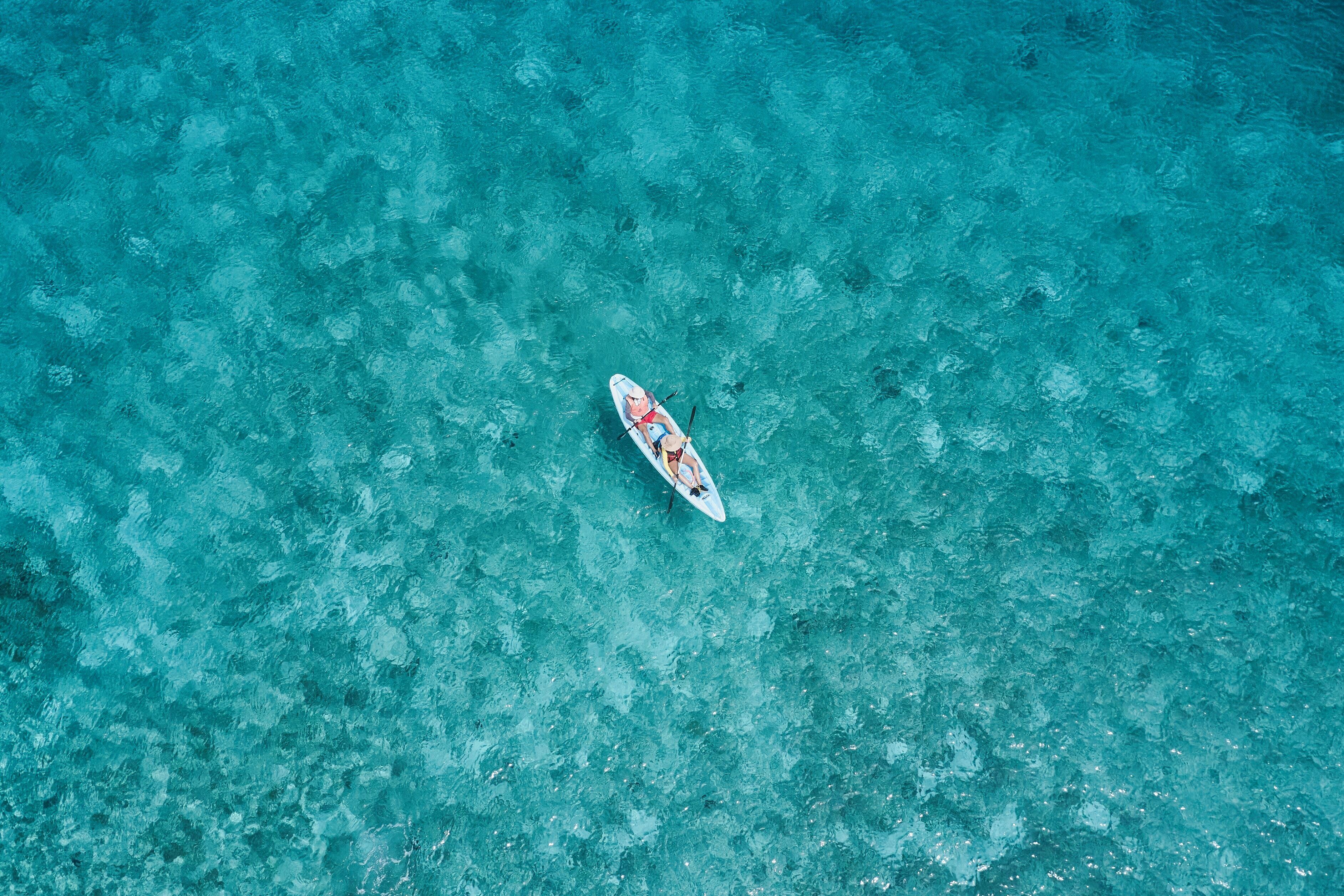 Une vue aérienne d’une mer turquoise et limpide, sur laquelle on aperçoit un seul bateau.