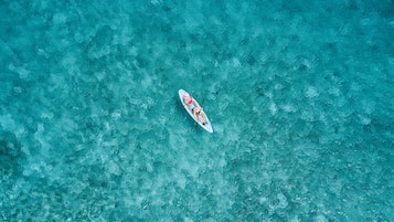 Une vue aérienne d’une mer turquoise et limpide, sur laquelle on aperçoit un seul bateau.
