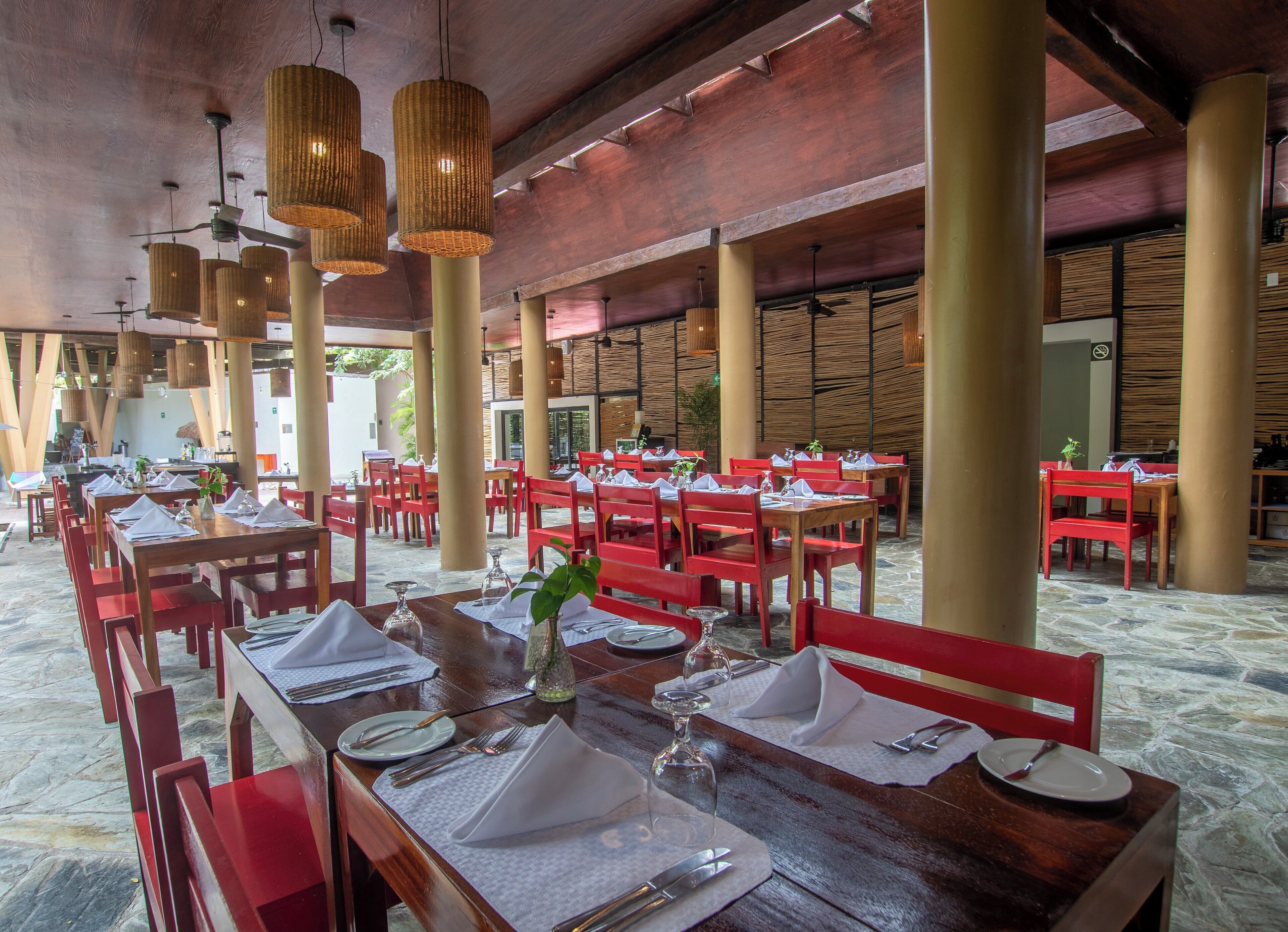 A spacious dining area with multiple tables set for dining, featuring red chairs and wooden tables.