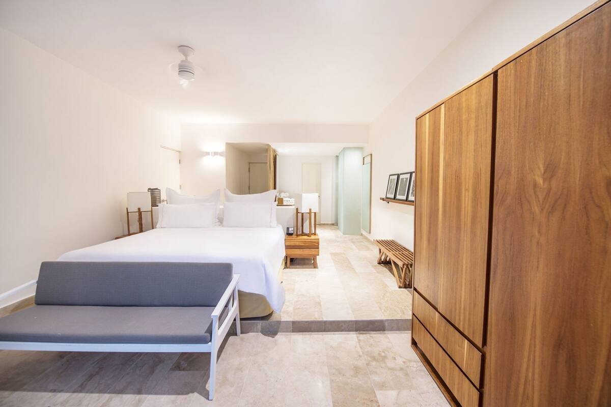Une chambre d’hôtel comprenant un lit, une table de chevet, une armoire et un banc.