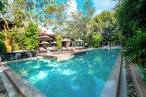 A swimming pool with lounge chairs and umbrellas, surrounded by lush greenery. - The Explorean Cozumel - All Inclusive (Cozumel)