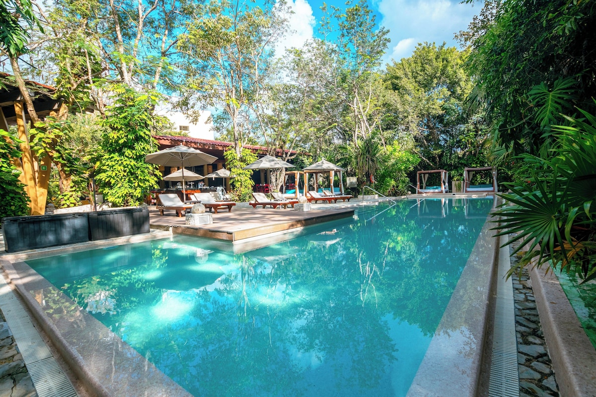A swimming pool with lounge chairs and umbrellas, surrounded by lush greenery. - The Explorean Cozumel - All Inclusive (Cozumel)